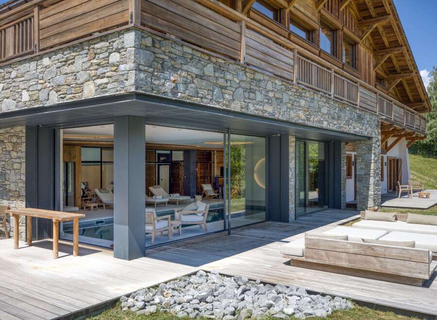 This luxury chalet boasts a seamless blend of rustic charm and modern design, featuring stone and wood exterior, expansive glass windows, and a tranquil indoor pool area.