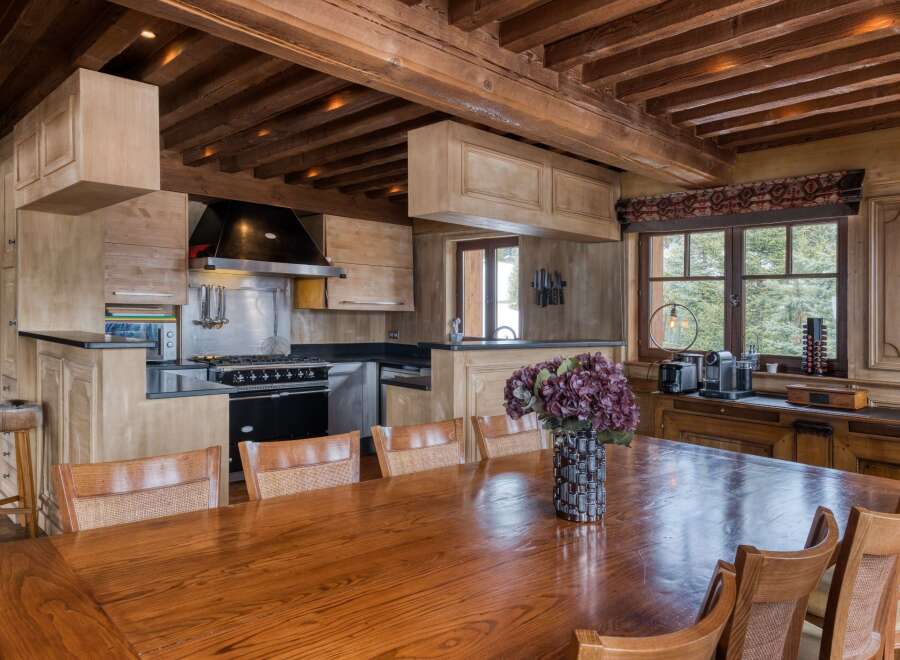 This inviting kitchen and dining area boasts rustic charm with exposed wooden beams and cabinetry, perfect for a cozy mountain retreat.