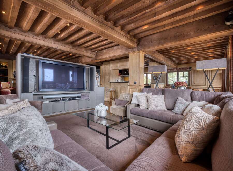 This luxurious living room boasts a stunning wooden beamed ceiling, a large comfortable sectional sofa, and a sleek glass coffee table.