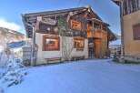 Charming chalet-style home with a wooden facade and cozy balcony, nestled in a snowy landscape.