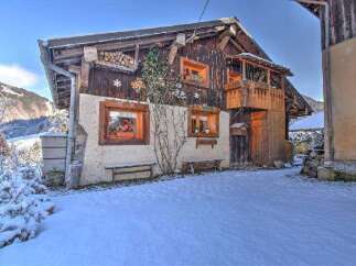 Charming chalet-style home with a wooden facade and cozy balcony, nestled in a snowy landscape.
