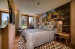 This luxurious bedroom features a king-size bed with plush linens, a stunning forest mural, and natural wood finishes.