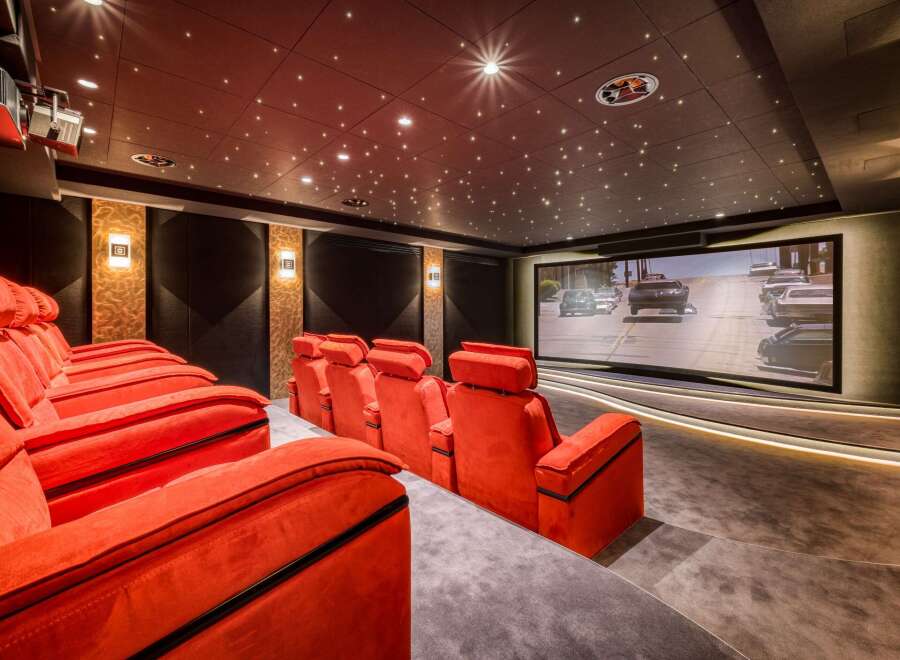 Experience the ultimate home theater with plush red seating, a high-definition screen displaying a car chase, and a mesmerizing star-lit ceiling.