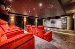 Experience the ultimate home theater with plush red seating, a high-definition screen displaying a car chase, and a mesmerizing star-lit ceiling.