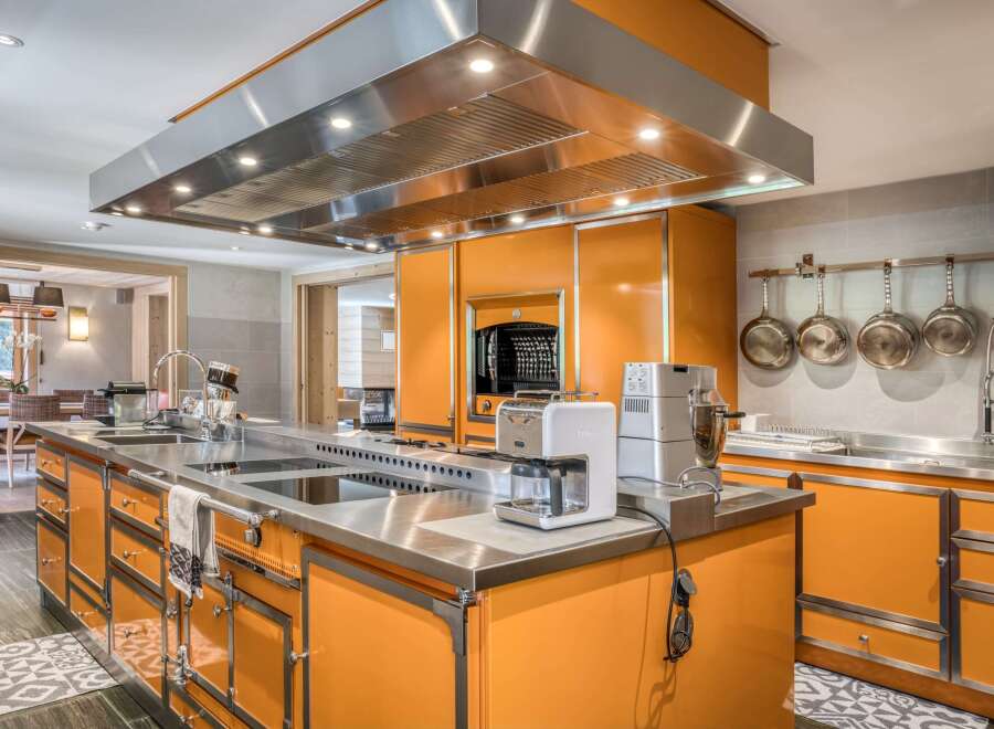 This bespoke kitchen boasts a vibrant orange cabinetry with stainless steel countertops and a range hood.