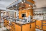 This bespoke kitchen boasts a vibrant orange cabinetry with stainless steel countertops and a range hood.