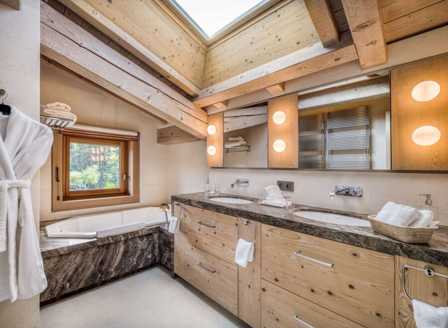 This luxurious bathroom features natural wood elements like exposed beams and a wooden vanity, complemented by a marble countertop and bathtub surround.