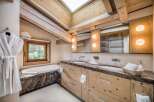 This luxurious bathroom features natural wood elements like exposed beams and a wooden vanity, complemented by a marble countertop and bathtub surround.