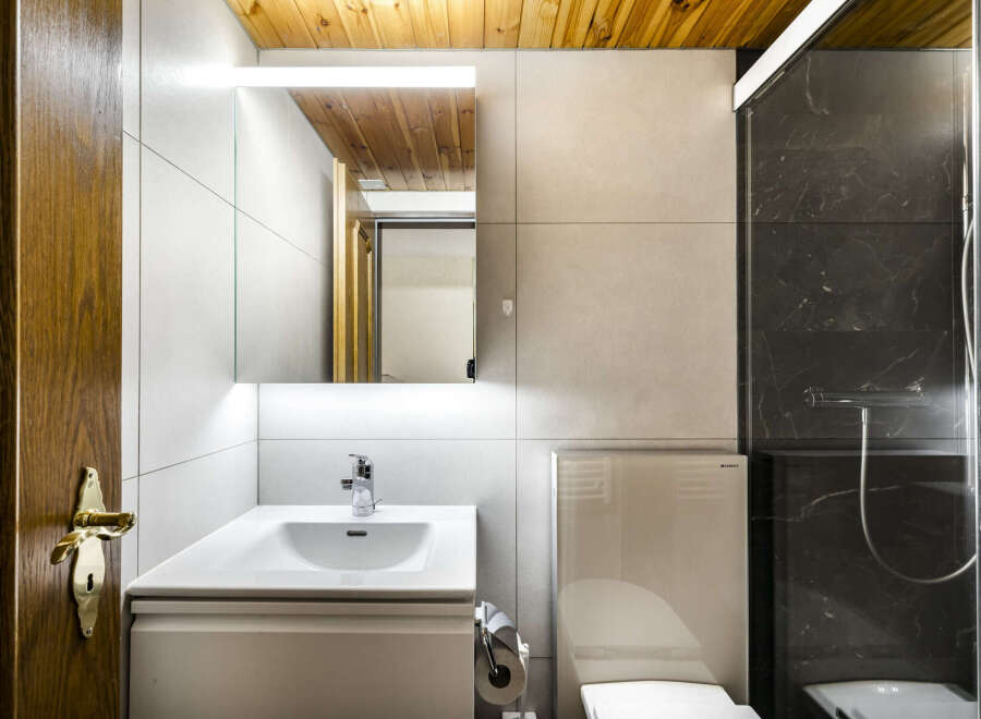 This modern bathroom features a sleek vanity with a white sink, a stylish mirror with integrated lighting, and a toilet with a concealed tank.