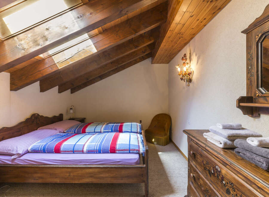 This charming attic bedroom boasts exposed wood beams, a skylight for natural light, and rustic wooden furniture.