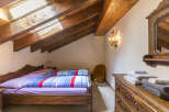 This charming attic bedroom boasts exposed wood beams, a skylight for natural light, and rustic wooden furniture.