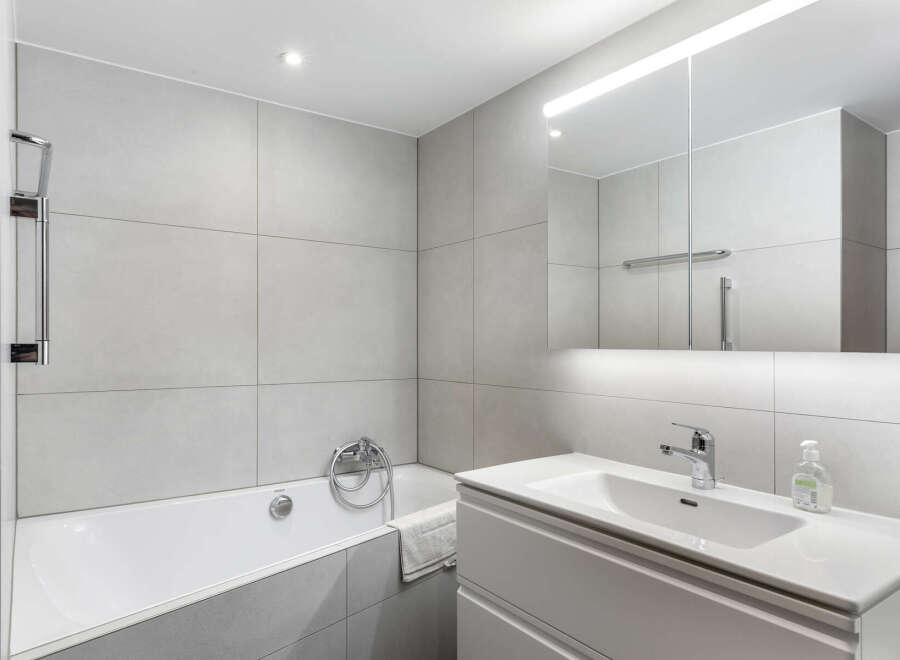 This modern bathroom boasts a sleek design with large, light gray tiles covering the walls, providing a clean and spacious feel.