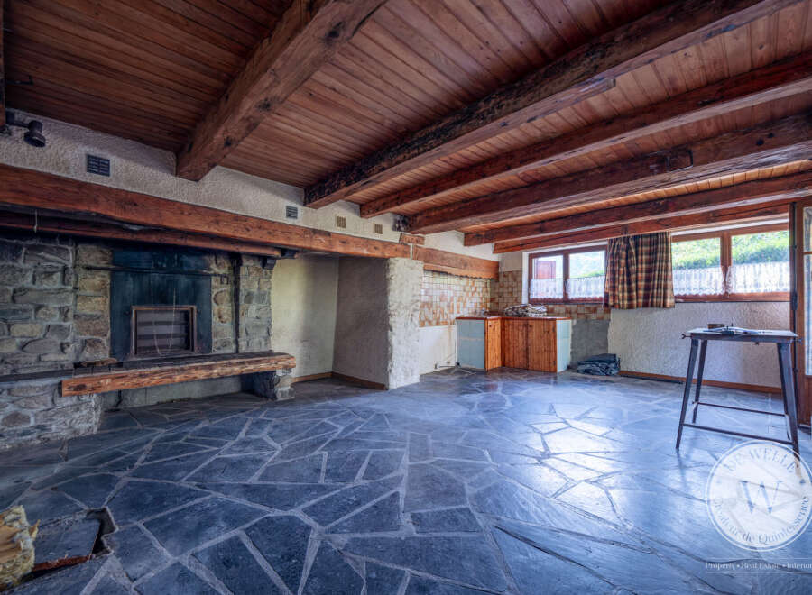 This interior showcases a rustic stone fireplace with a wooden mantel, complemented by a unique floor of irregularly shaped dark tiles.