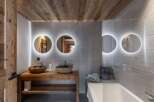 This bathroom features a rustic wooden vanity with stone vessel sinks, illuminated round mirrors, and a modern bathtub.