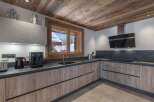 This kitchen features wooden cabinets with sleek, modern hardware and a dark countertop that contrasts beautifully with the light walls.