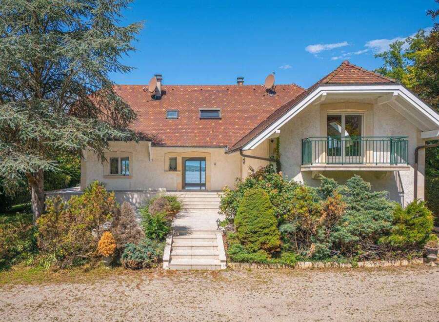 An elegant two-story house with a unique red-tiled roof, complemented by a balcony and lush greenery.