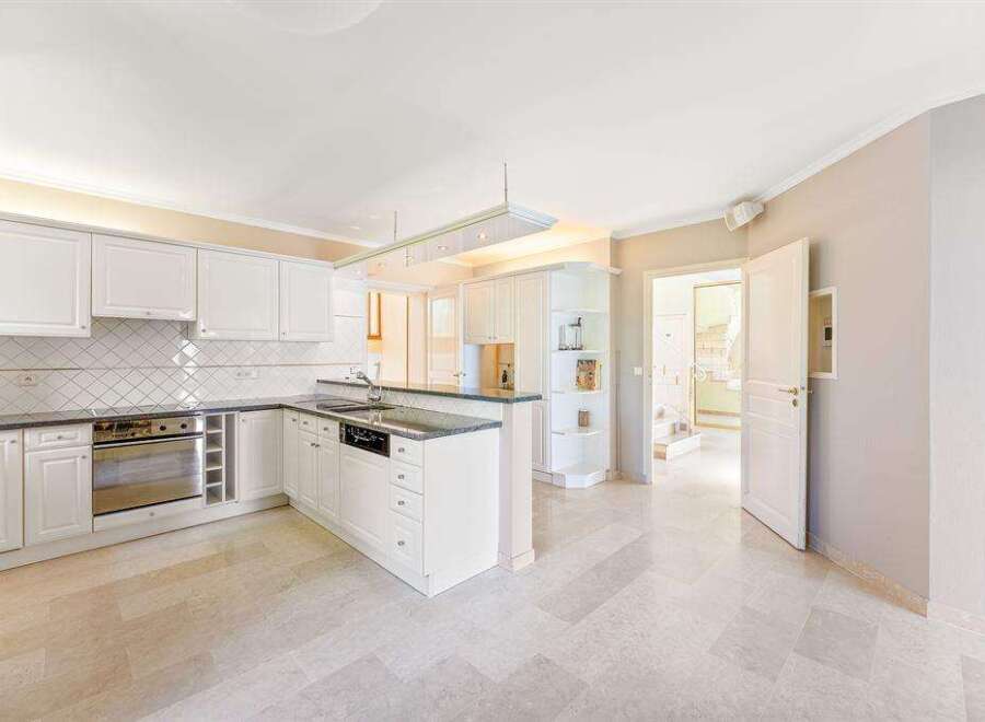 This spacious kitchen features sleek white cabinetry, stainless steel appliances, and a functional island with bar seating, perfect for modern living.