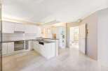 This spacious kitchen features sleek white cabinetry, stainless steel appliances, and a functional island with bar seating, perfect for modern living.