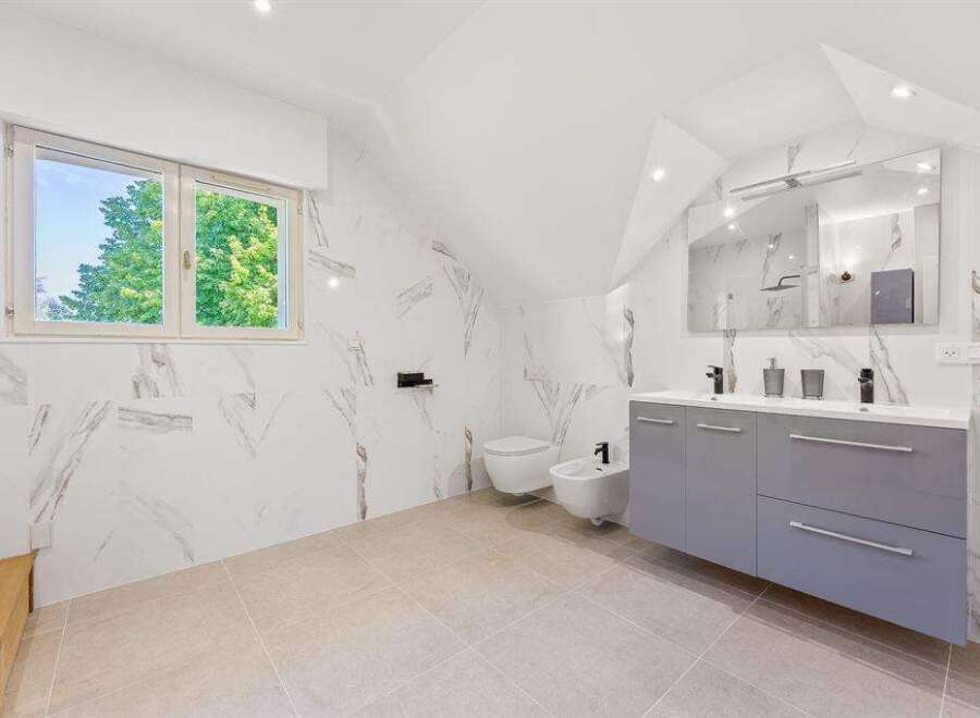 This modern bathroom features stunning marble-effect walls, a sleek grey double vanity, and a bidet for added convenience.