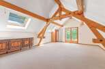 A spacious attic room featuring exposed wooden beams, skylights that flood the space with natural light, and elegant French doors opening to a balcony.