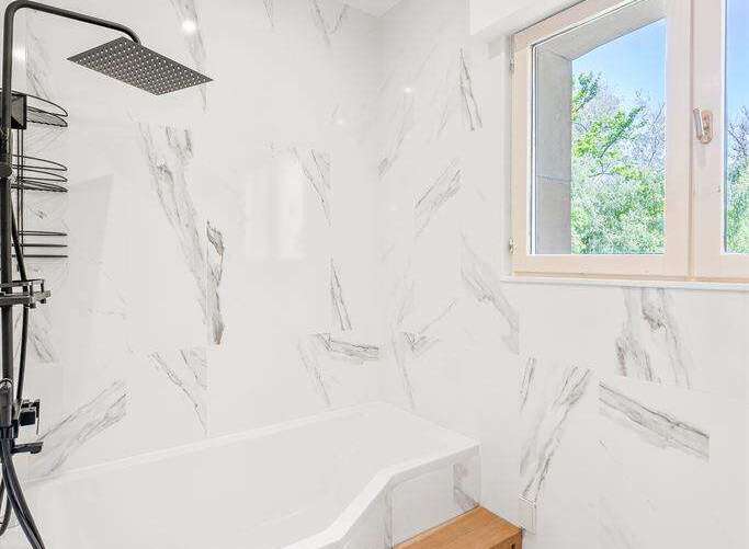 This is a modern bathroom featuring white marble-patterned walls and a matching white bathtub.
