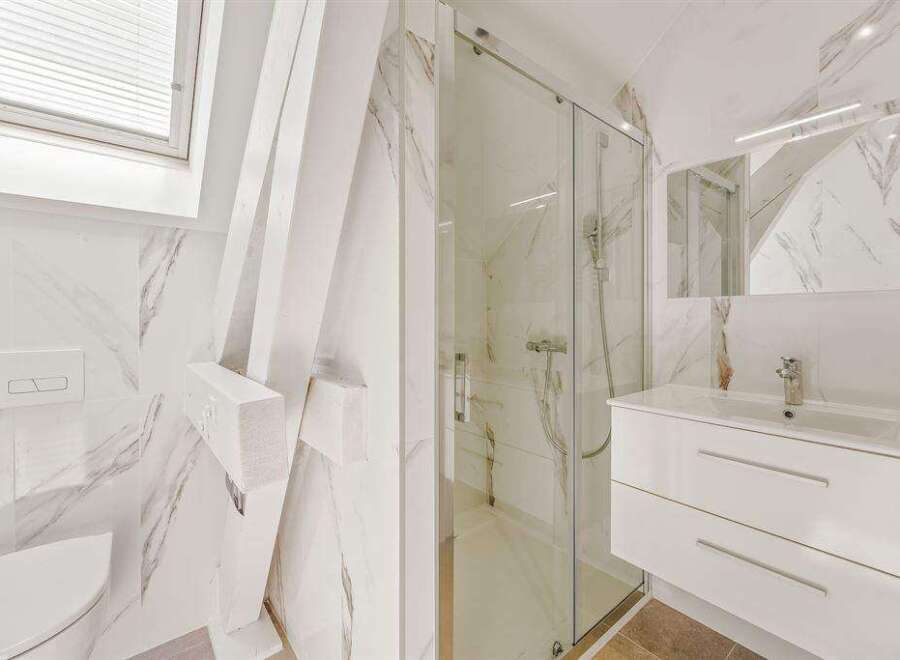 This modern bathroom features stylish marble-effect tiling, complemented by a sleek white vanity and a glass-enclosed shower.