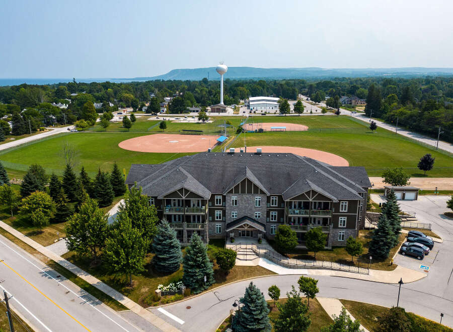 Discover this charming apartment complex with a view of a sports field and water tower, nestled near lush trees.