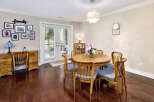 This inviting dining area features rich hardwood floors, a charming round wooden table with blue cushioned chairs, and a stylish chandelier.