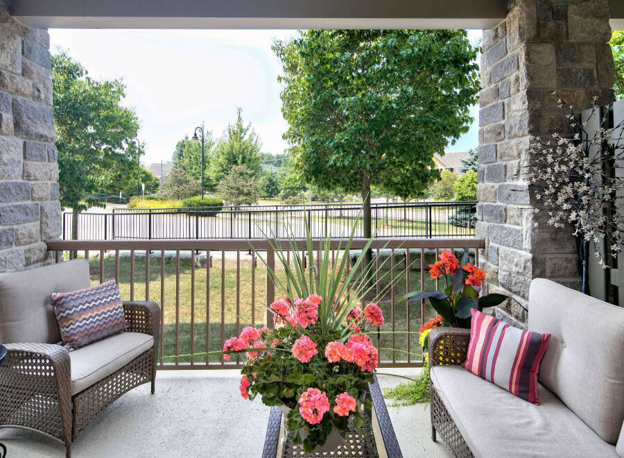 Enjoy outdoor living on this charming porch featuring stone pillars, comfortable wicker seating, and vibrant floral arrangements.