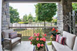 Enjoy outdoor living on this charming porch featuring stone pillars, comfortable wicker seating, and vibrant floral arrangements.