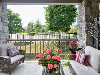 Enjoy outdoor living on this charming porch featuring stone pillars, comfortable wicker seating, and vibrant floral arrangements.
