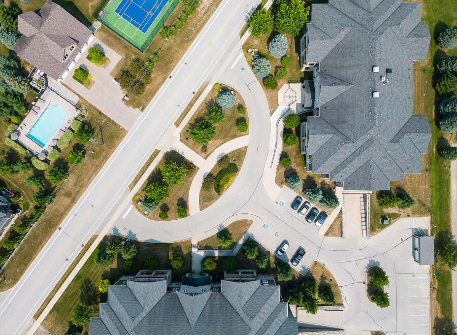 An aerial view captures a well-maintained property featuring a swimming pool, tennis court, and ample parking.