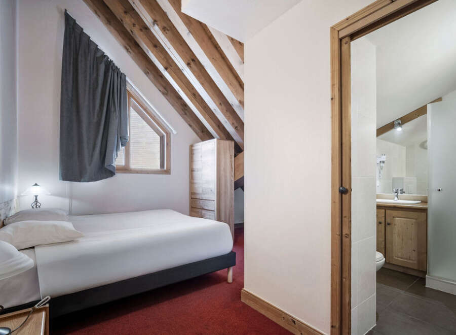 Discover the charm of this cozy bedroom, featuring a comfortable bed and a unique sloped ceiling with exposed wooden beams.