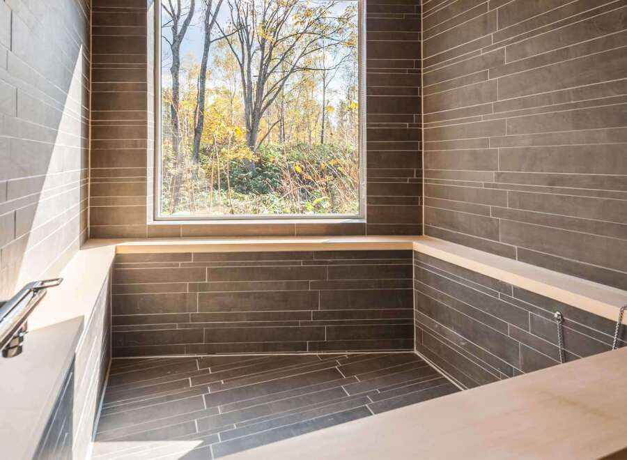Experience tranquility in this luxurious bathroom, featuring a stunning view of nature through a large window.