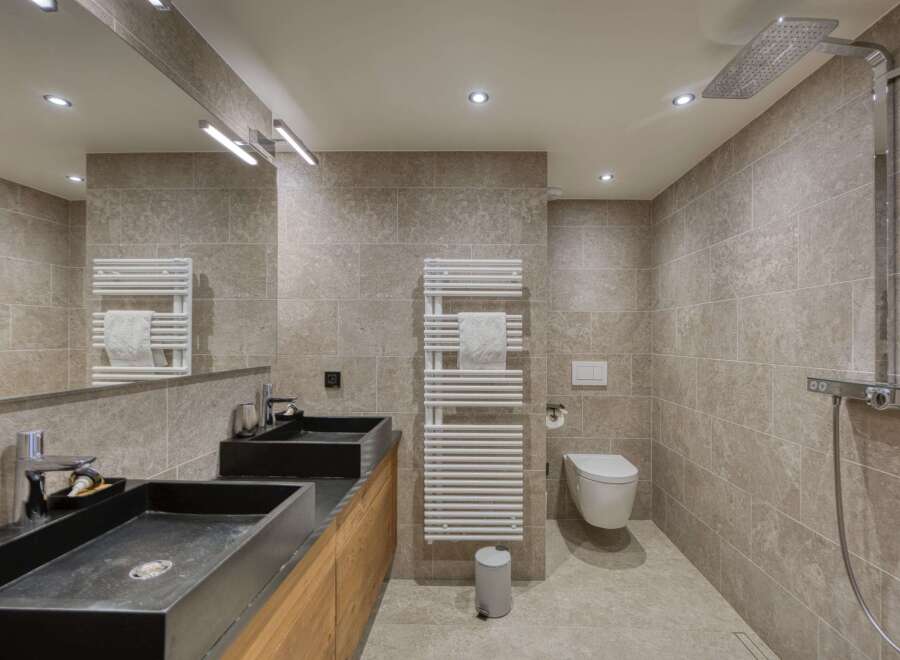 This modern bathroom boasts a sleek design with its dark sinks and neutral-toned tiles.