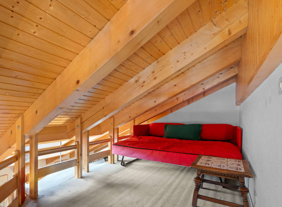 This charming loft space features a cozy red sofa and a unique wooden beam ceiling, creating a warm and inviting atmosphere.