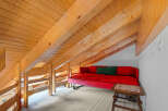 This charming loft space features a cozy red sofa and a unique wooden beam ceiling, creating a warm and inviting atmosphere.