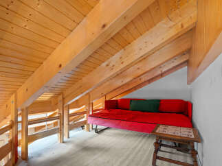 This charming loft space features a cozy red sofa and a unique wooden beam ceiling, creating a warm and inviting atmosphere.