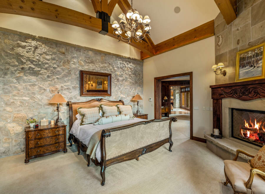 Experience luxury in this stunning bedroom featuring a stone accent wall and a cozy fireplace.