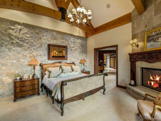 Experience luxury in this stunning bedroom featuring a stone accent wall and a cozy fireplace.