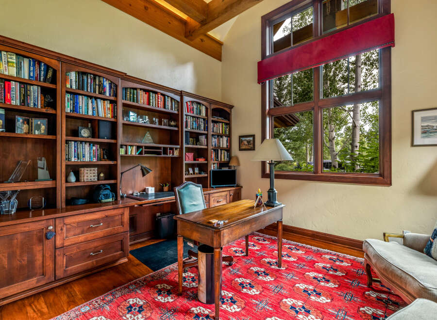 Step into luxury with this stunning home office, featuring custom built-in bookshelves, a classic desk, and a vibrant red rug.