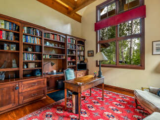 Step into luxury with this stunning home office, featuring custom built-in bookshelves, a classic desk, and a vibrant red rug.