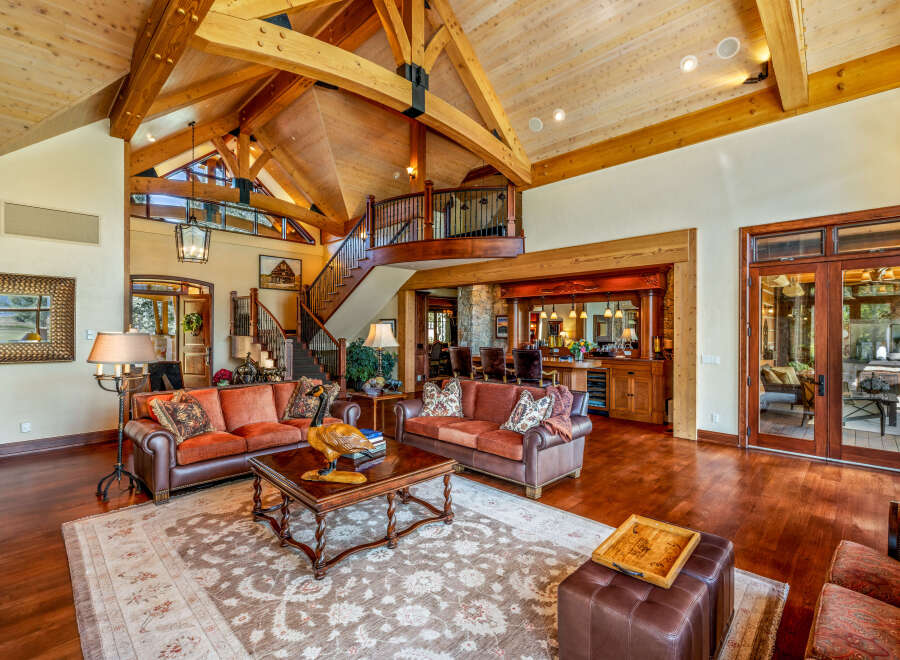 Experience luxury living in this stunning property, featuring a grand living room with soaring ceilings and exposed wooden beams.