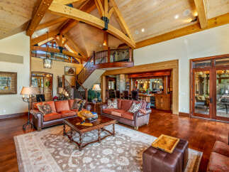 Experience luxury living in this stunning property, featuring a grand living room with soaring ceilings and exposed wooden beams.