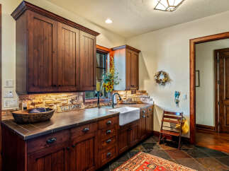 This stunning kitchen boasts custom wood cabinetry, a farmhouse sink, and a beautiful stone backsplash, creating a warm and inviting atmosphere.