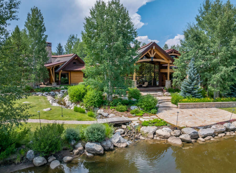 This stunning property showcases a luxurious home nestled amidst lush landscaping and a serene pond.