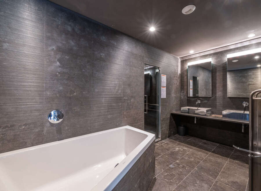 This luxurious bathroom features a sleek, modern design with dark gray textured walls and a pristine white bathtub.