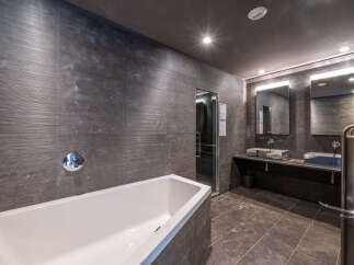 This luxurious bathroom features a sleek, modern design with dark gray textured walls and a pristine white bathtub.