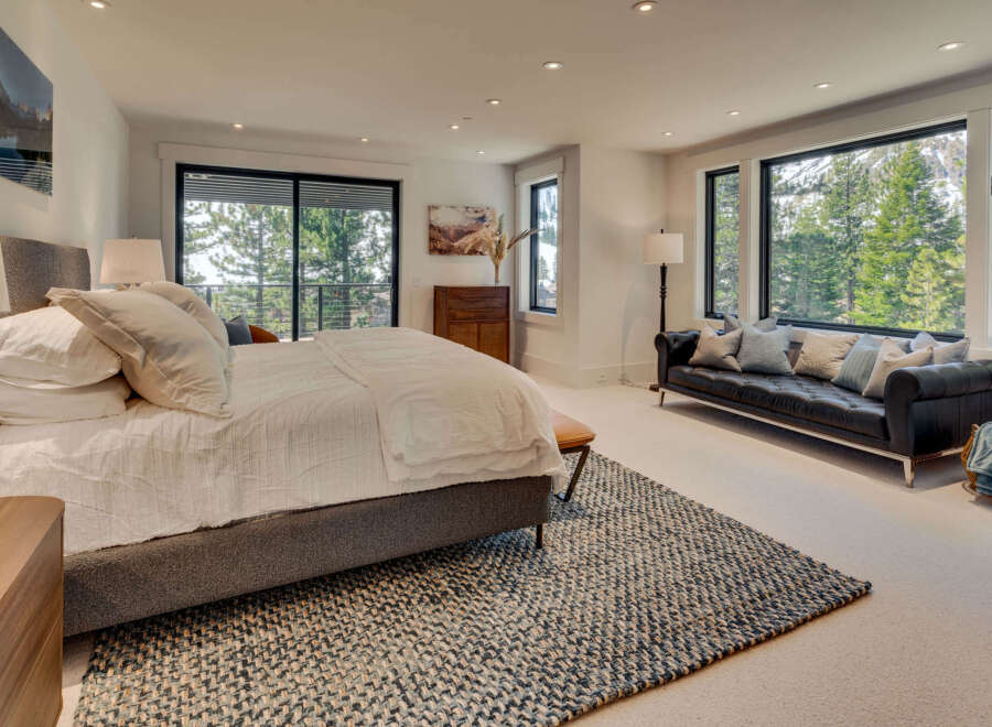Experience luxury in this stunning bedroom featuring a plush bed, a stylish black leather sofa, and expansive windows that frame breathtaking views of the surrounding nature.
