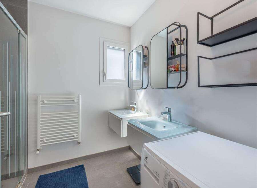 This modern bathroom features a sleek design with a double sink vanity and a washing machine.
